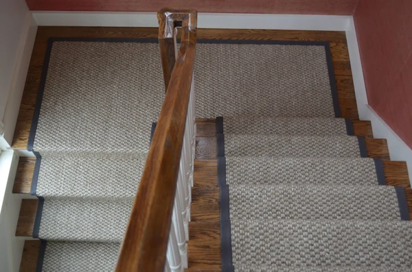 Textured neutral stair runner with dark border on wooden stairs.