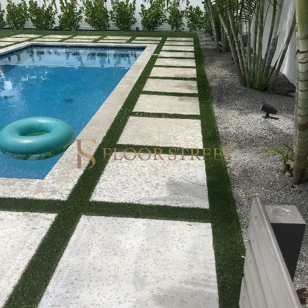 Artificial grass carpet installed between large stone pavers lining a swimming pool.