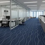 Blue patterned carpet tiles with a wavy, rippling design in a modern office hallway.