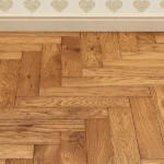 Classic oak herringbone flooring against a white wall.