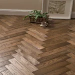 Dark herringbone wood flooring styled with a plant.