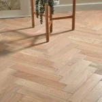 Light oak flooring in a herringbone pattern with a plant stand.