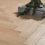 Light oak herringbone wood floor with a decorative plant and books.