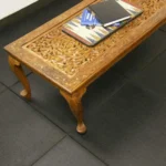 Ornate wooden coffee table on black rubber floor tiles.