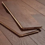 Two planks of dark brown wood flooring resting on an installed dark wood floor.