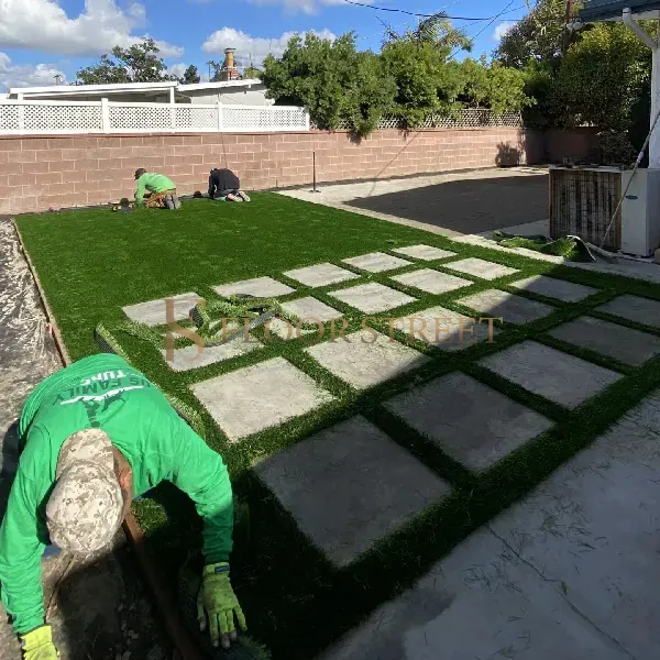 Workers installing artificial turf around square stone pavers