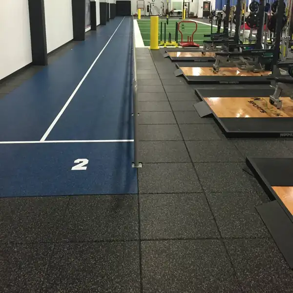 black rubber gym flooring tiles installed alongside a blue sprint