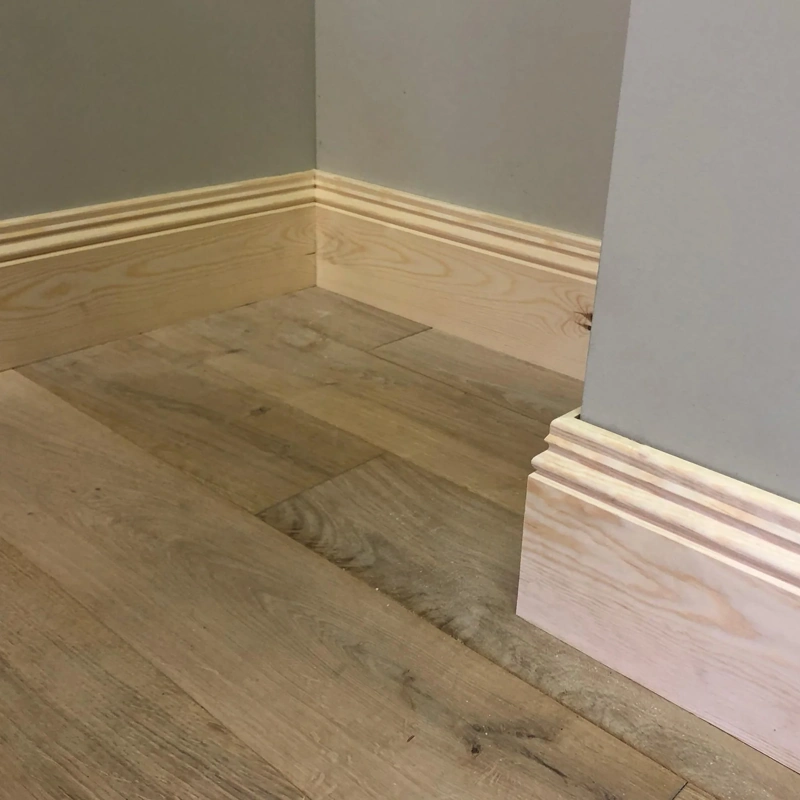 Pine skirting board against a grey painted wall.