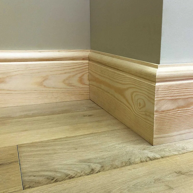 Rounded pine skirting board against a grey wall.